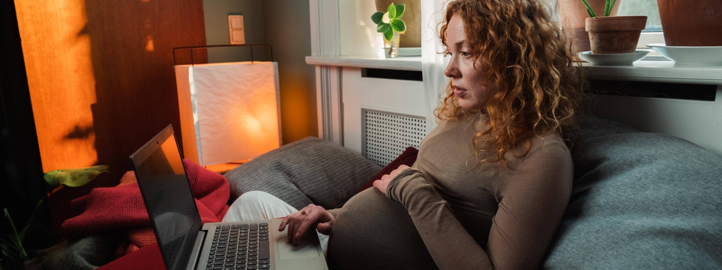 Gravid kvinde sidder i sofa og kigger på en PC