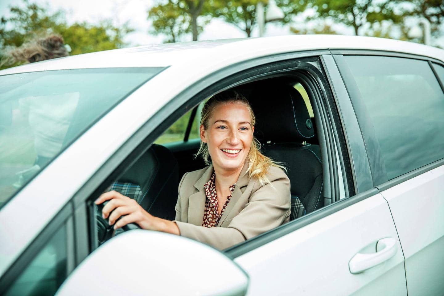 Kvinde sidder bag rattet på en bil og smiler