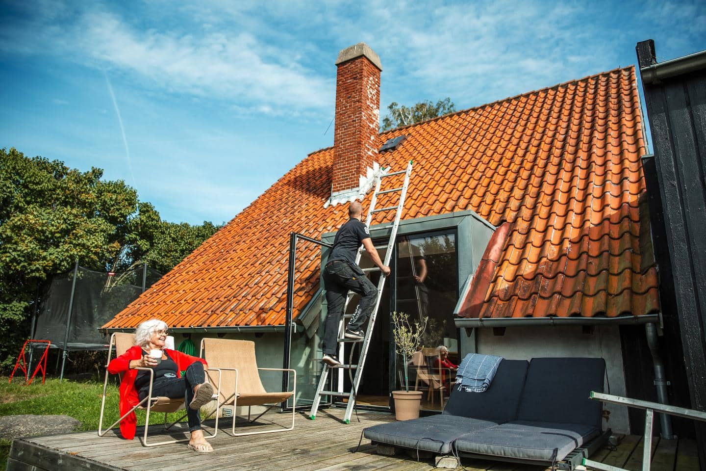 Kvinde sidder på terrassen mens håndværkeren arbejder på taget.