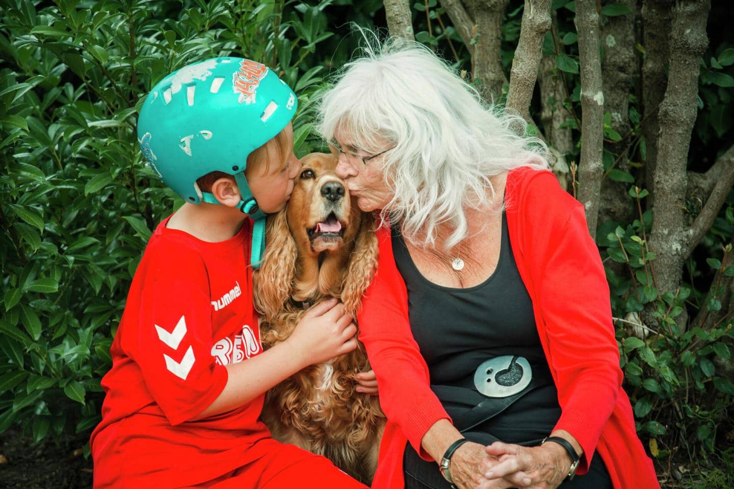 Dreng med cykelhjelm og ældre kvinde kysser hund
