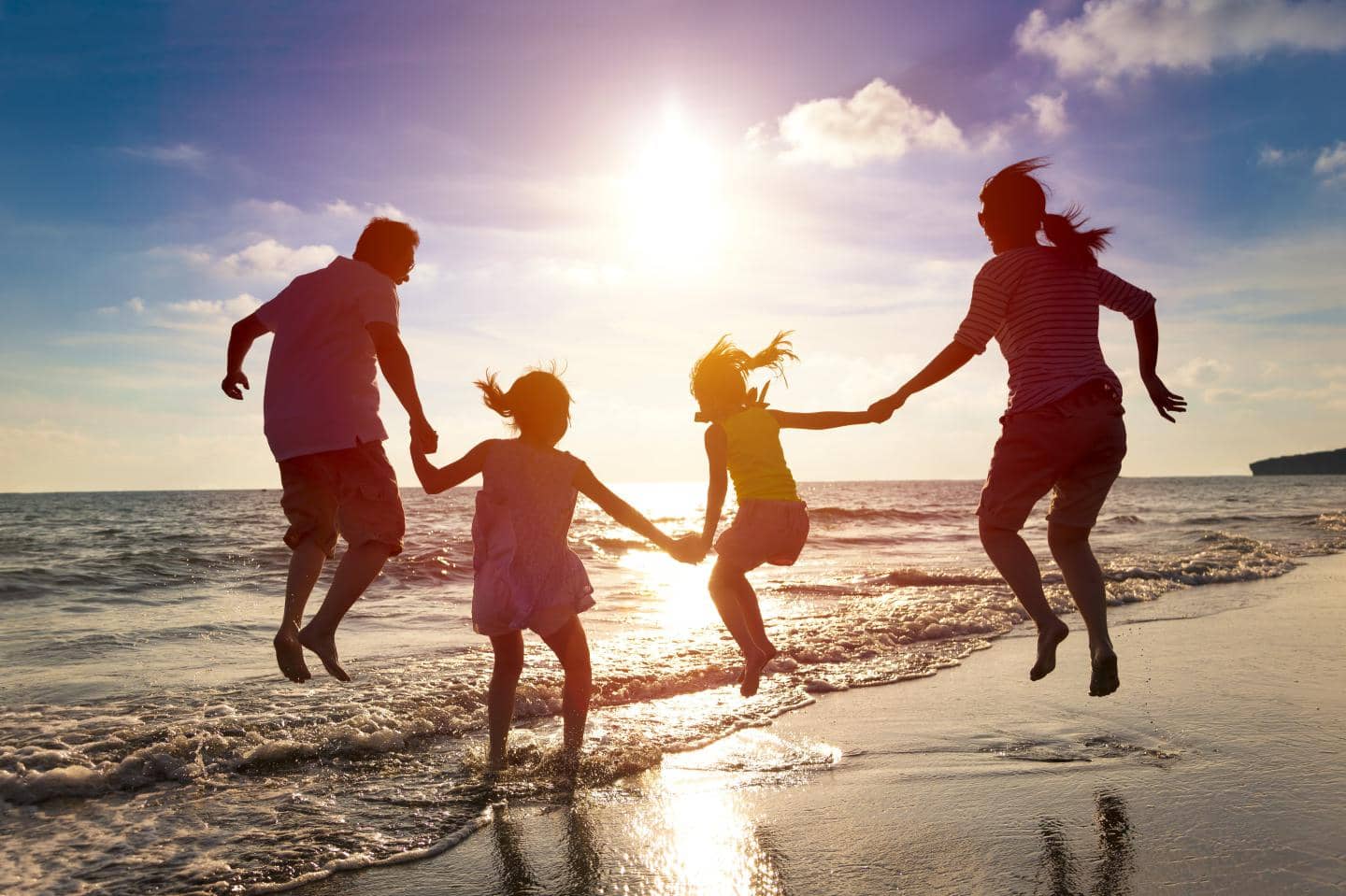 Familie på stranden ved solnedgang hopper imens de holder hinanden i hånden