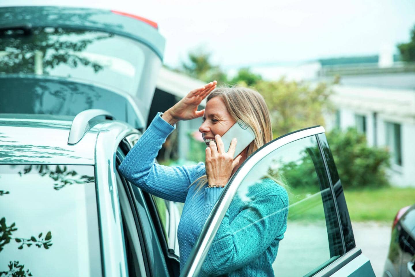 Kvinde står ved sin bil og taler smilende i telefon