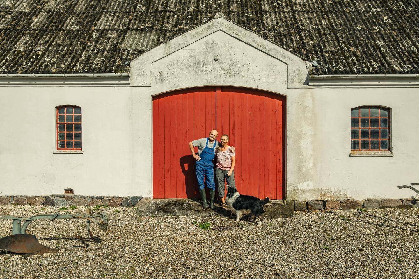En mand og en kvinde samt en hund foran porten til en landejendom